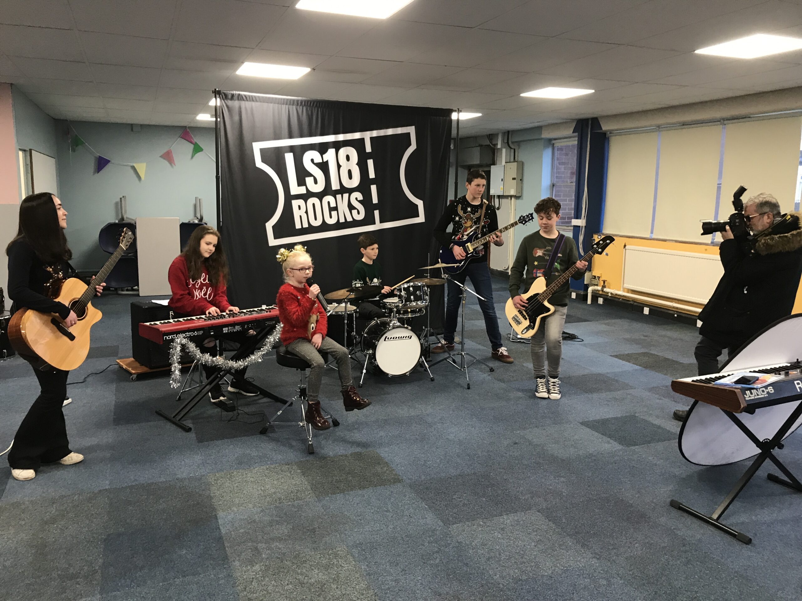 The LS18 Rocks project band playing together: children and young people of various ages playing guitar, piano and drums with a singer.