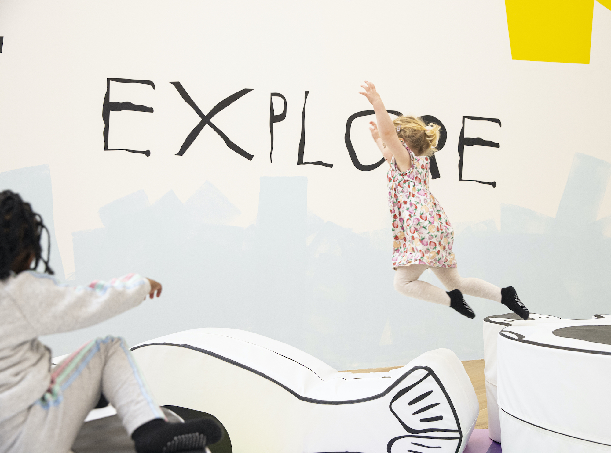 A young child leaps, with the word 'Explore' painted in the background