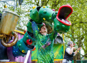 A green dragon puppet operated by a puppeteer dressed in green at an outdoor event