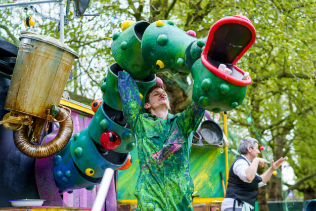 A green dragon puppet operated by a puppeteer dressed in green at an outdoor event