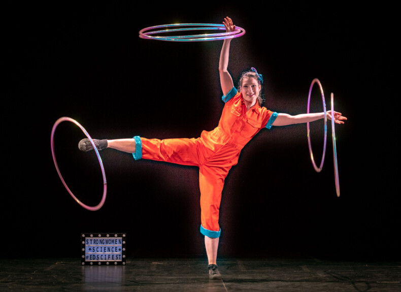 A circus performer balancing rings on her arms and right leg, on stage at the Strong Women Science show.