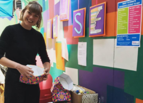 Person smiles whilst holding a paper crafted coloured container