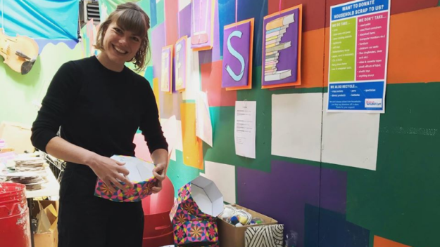 Person smiles whilst holding a paper crafted coloured container