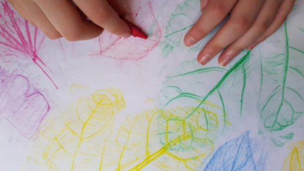 Hand holding a red crayon resting on a print of leaves